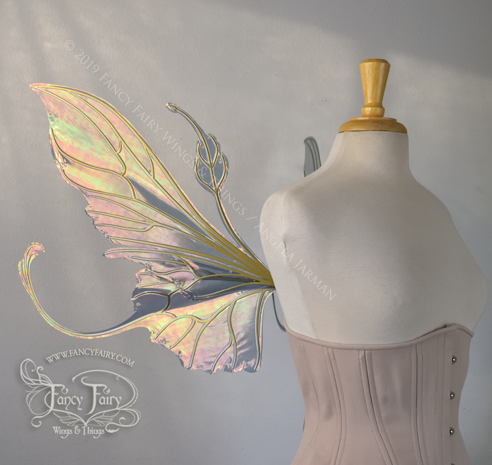 Left side view of an ivory dress form wearing an alabaster underbust corset & large orange/green iridescent fairy wings with elongated upper panels & antennae with bottom panels that have a tail curving upwards, gold veins