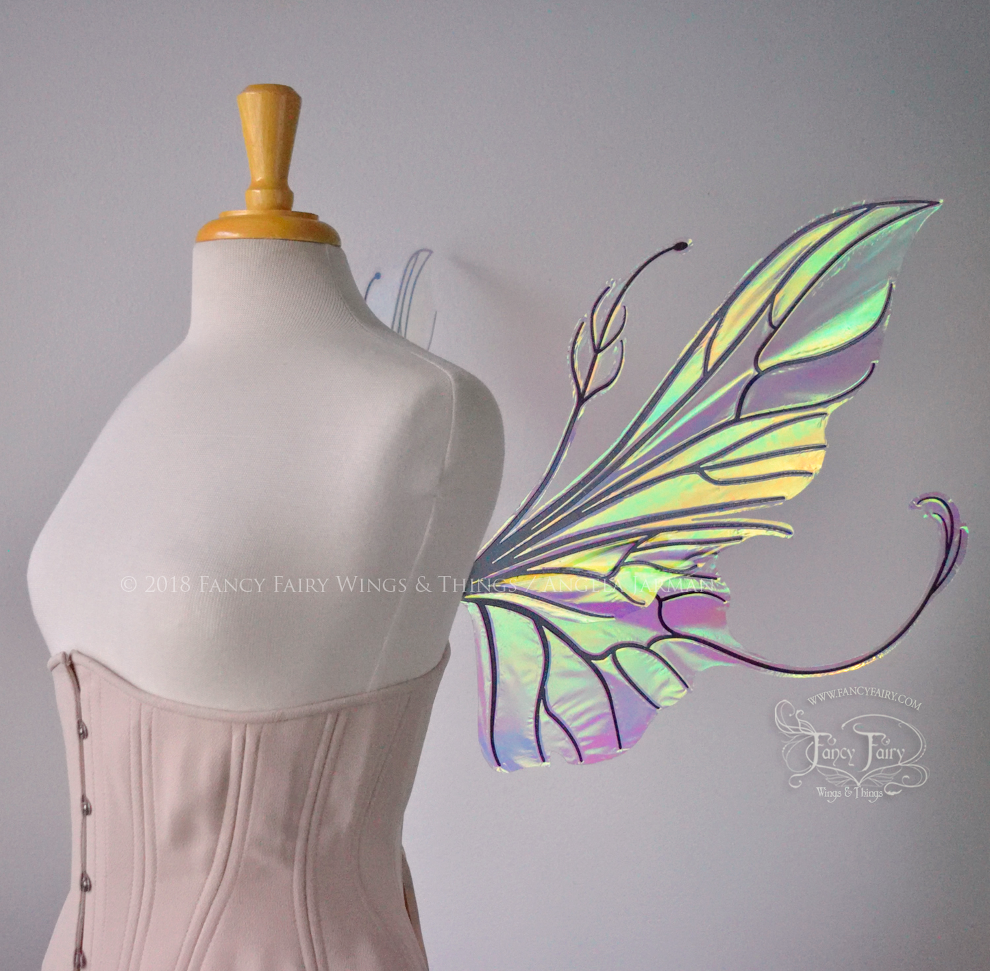 Right side view of an ivory dress form wearing an alabaster underbust corset & large clear iridescent fairy wings with elongated upper panels & antennae with bottom panels that have a tail curving upwards, black veins