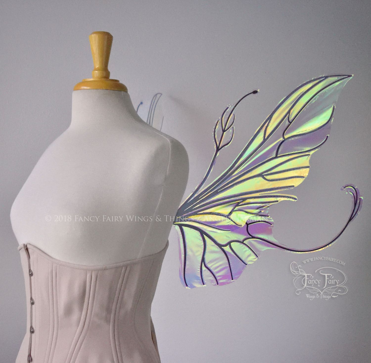 Right side view of an ivory dress form wearing an alabaster underbust corset & large clear iridescent fairy wings with elongated upper panels & antennae with bottom panels that have a tail curving upwards, black veins