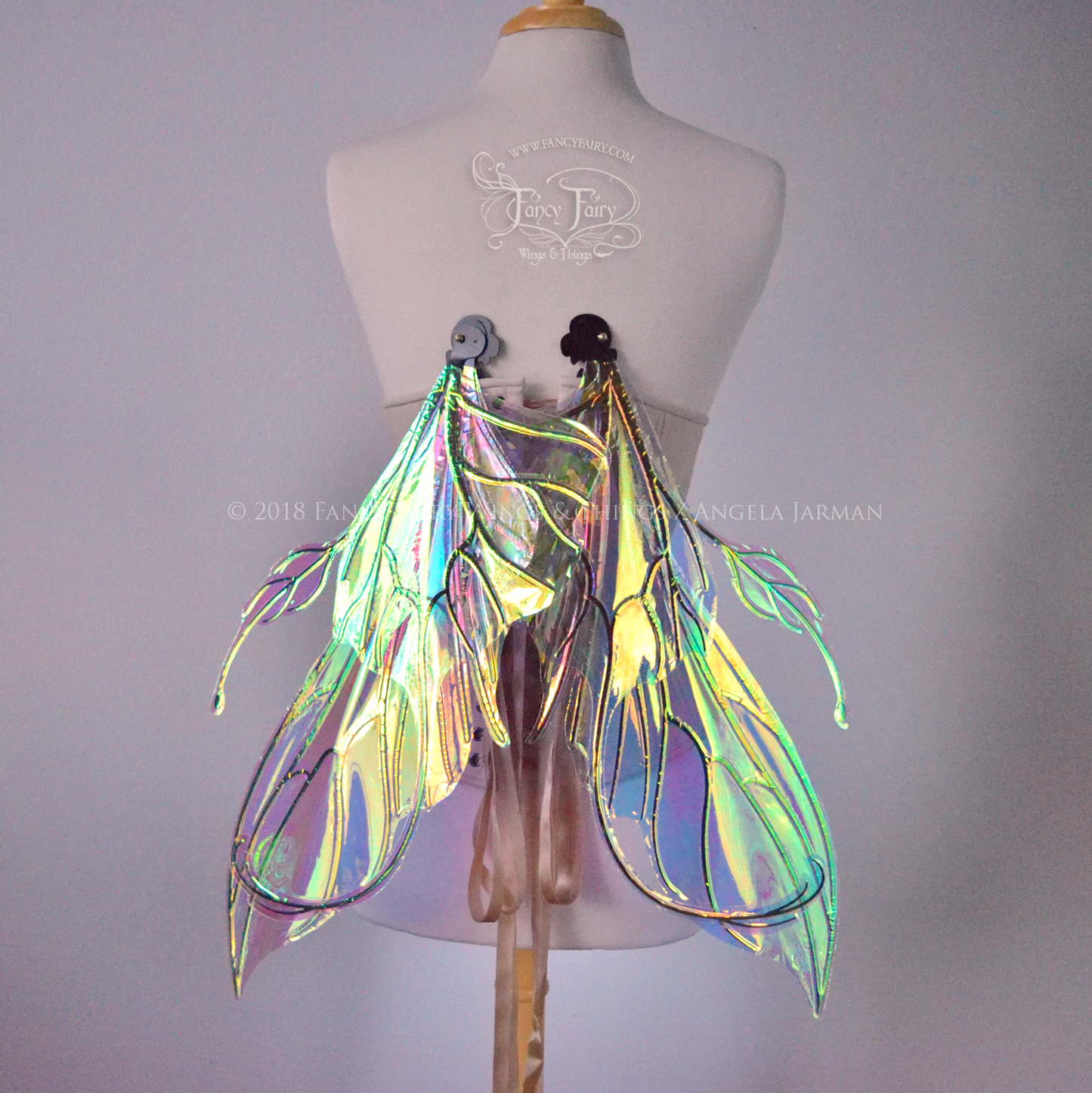 Back view of an ivory dress form wearing an alabaster underbust corset & large clear iridescent fairy wings with elongated upper panels & antennae with bottom panels that have a tail curving upwards, in a downwards resting position with black veins