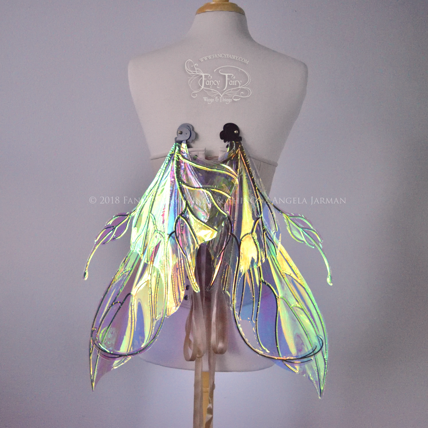 Back view of an ivory dress form wearing an alabaster underbust corset & large clear iridescent fairy wings with elongated upper panels & antennae with bottom panels that have a tail curving upwards, in a downwards resting position with black veins