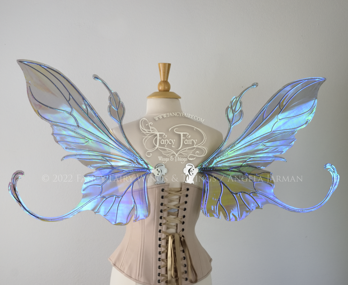 Back view of an ivory dress form wearing an alabaster underbust corset & large purple/blue iridescent fairy wings with elongated upper panels & antennae with bottom panels that have a tail curving upwards, silver veins