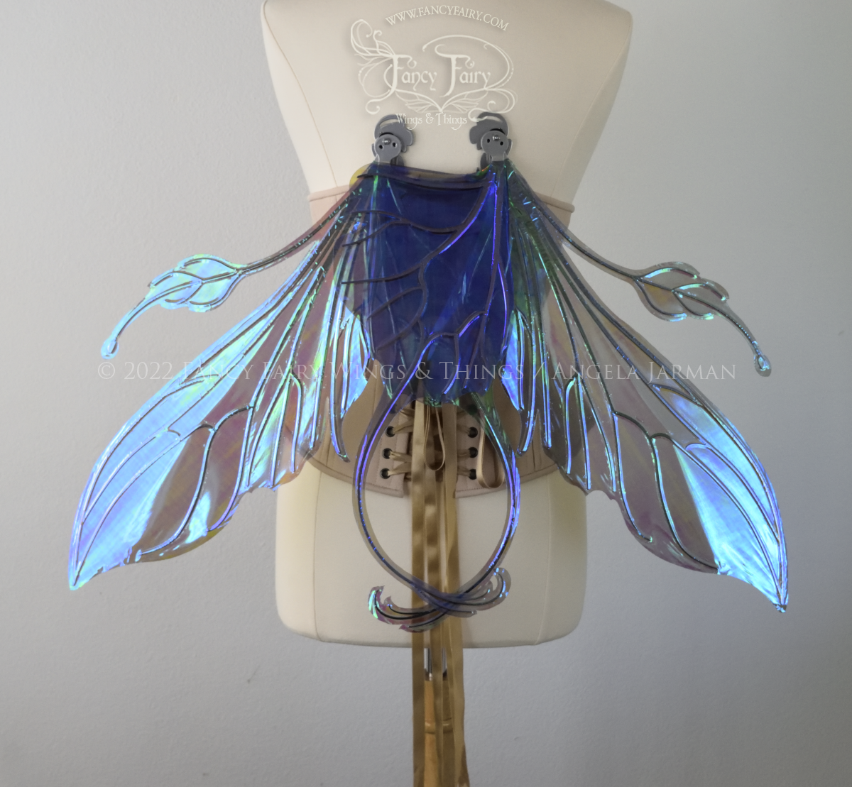 Back view of an ivory dress form wearing an alabaster underbust corset & large purple/blue iridescent fairy wings with elongated upper panels & antennae with bottom panels that have a tail curving upwards, silver veins, in resting position