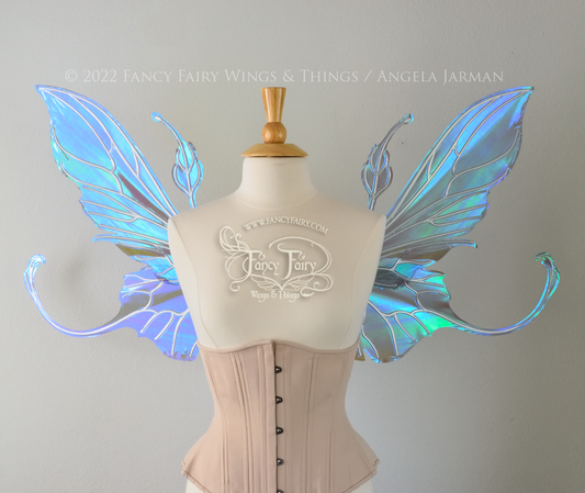 Front view of an ivory dress form wearing an alabaster underbust corset & large purple/blue iridescent fairy wings with elongated upper panels & antennae with bottom panels that have a tail curving upwards, silver veins