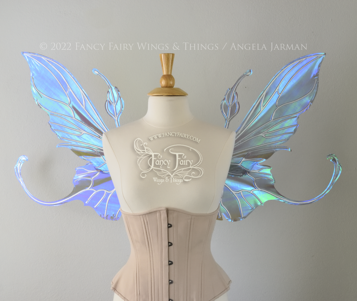Front view of an ivory dress form wearing an alabaster underbust corset & large purple/blue iridescent fairy wings with elongated upper panels & antennae with bottom panels that have a tail curving upwards, silver veins