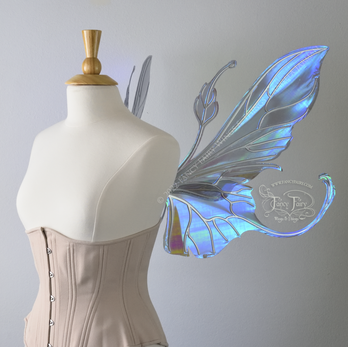 Right side view of an ivory dress form wearing an alabaster underbust corset & large purple/blue iridescent fairy wings with elongated upper panels & antennae with bottom panels that have a tail curving upwards, silver veins