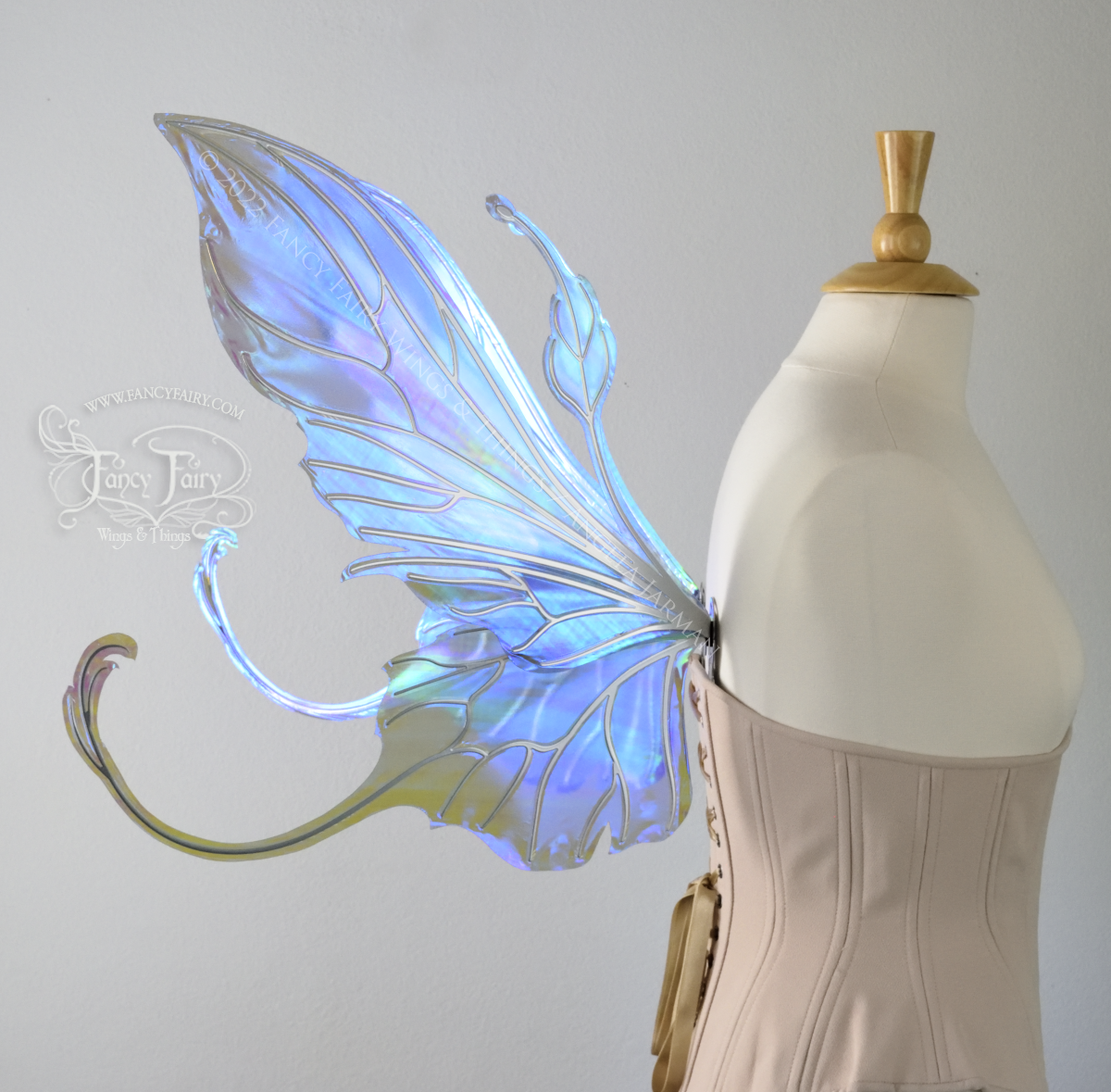 Left side view #2 of an ivory dress form wearing an alabaster underbust corset & large purple/blue iridescent fairy wings with elongated upper panels & antennae with bottom panels that have a tail curving upwards, silver veins