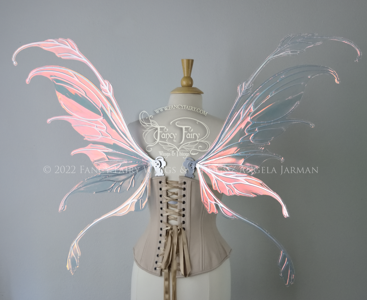 Back view of a dress form wearing an underbust corset & 'Fauna' transparent pink iridescent fairy wings with downward curved tips, antennae & wispy 'tails', with silver veining
