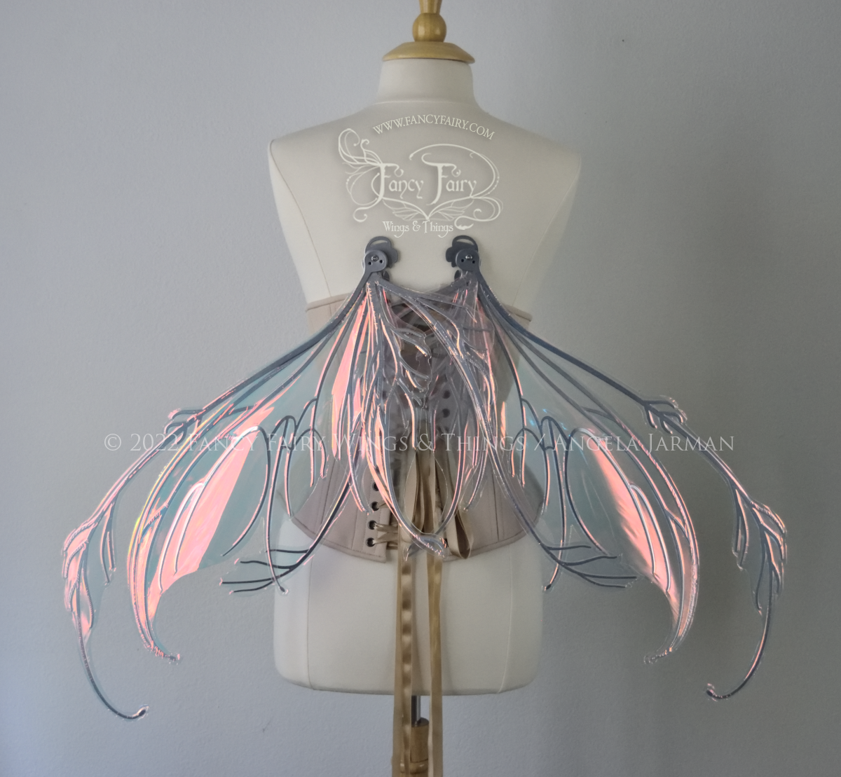 Back view of a dress form wearing an underbust corset & 'Fauna' transparent pink iridescent fairy wings with downward curved tips, antennae & wispy 'tails', with silver veining, in resting position
