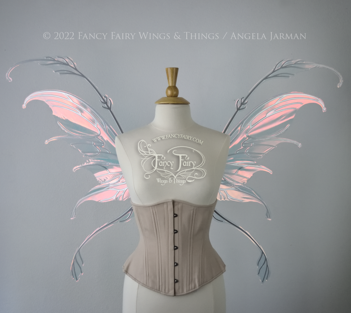 Front view of a dress form wearing an underbust corset & 'Fauna' transparent pink iridescent fairy wings with downward curved tips, antennae & wispy 'tails', with silver veining