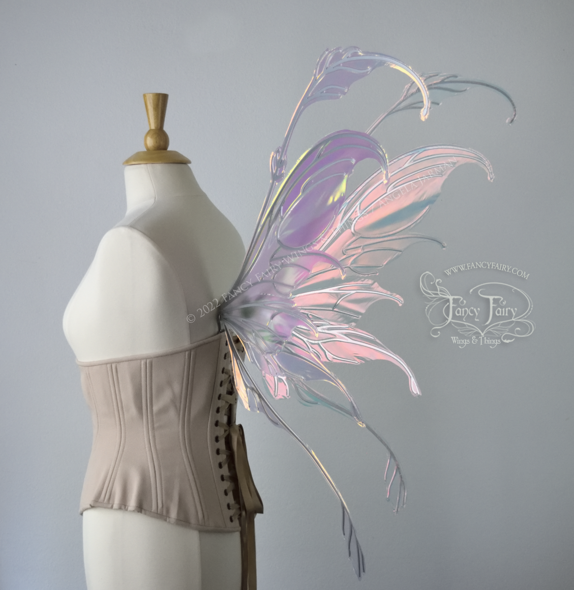 Back 3/4 side view of a dress form wearing an underbust corset & 'Fauna' transparent pink iridescent fairy wings with downward curved tips, antennae & wispy 'tails', with silver veining
