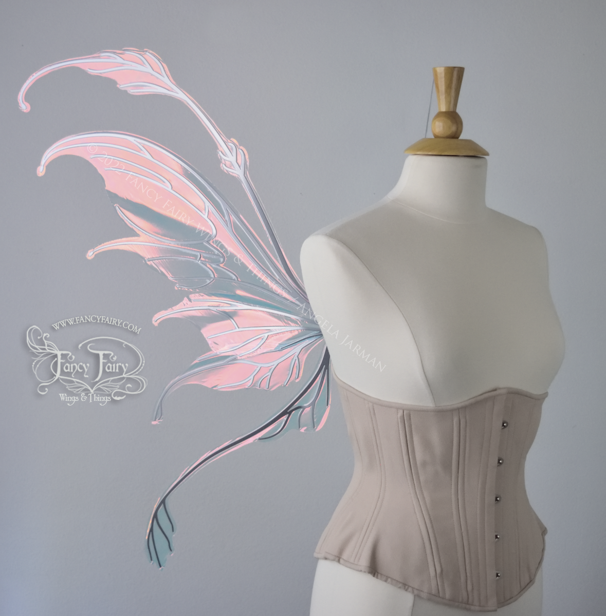 Left side view of a dress form wearing an underbust corset & 'Fauna' transparent pink iridescent fairy wings with downward curved tips, antennae & wispy 'tails', with silver veining