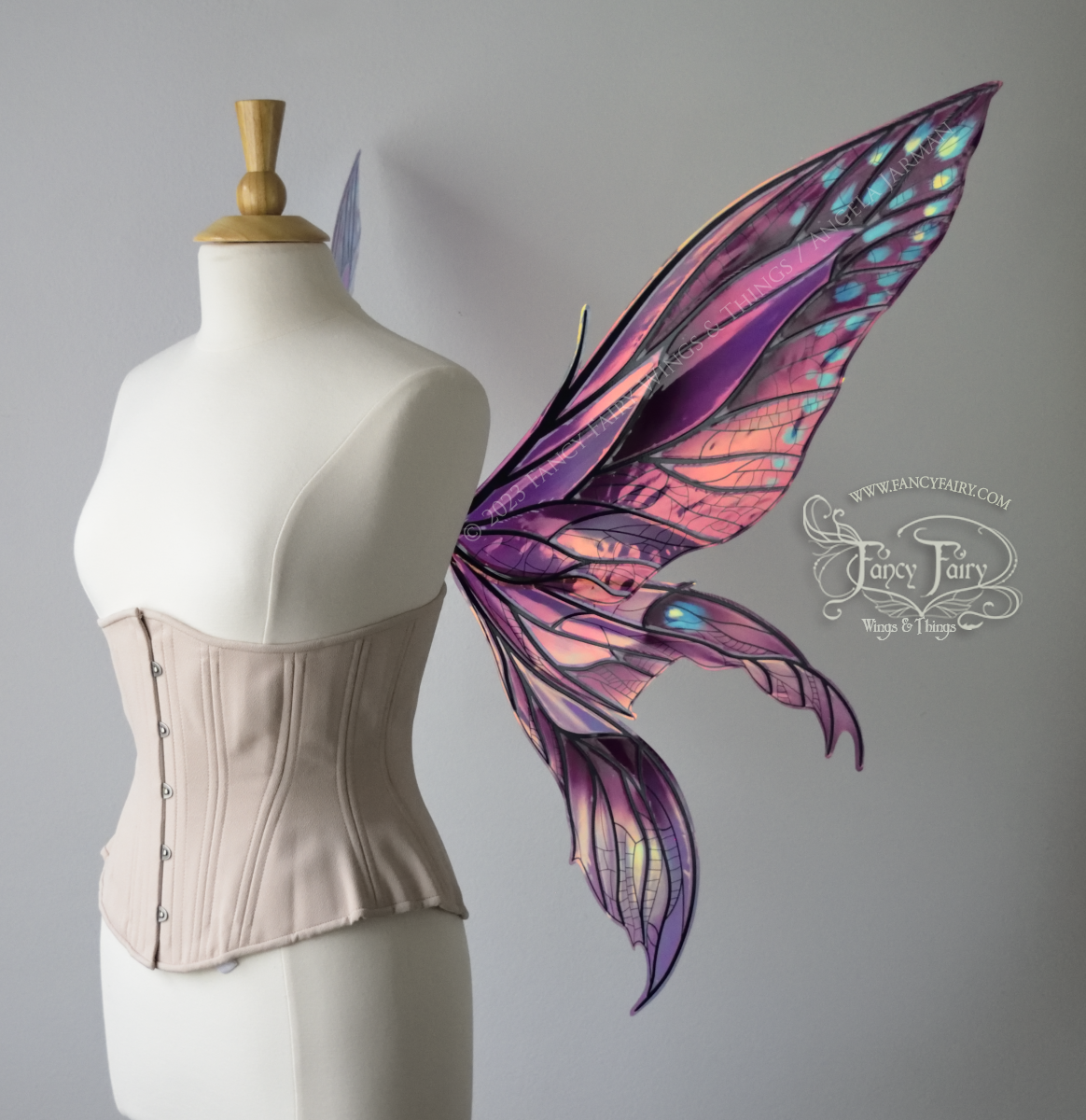 Right side view of large burgundy and peach pink iridescent fairy wings with 3 panels on each side, pointed tips, lots of vein detail, worn on a dress form.