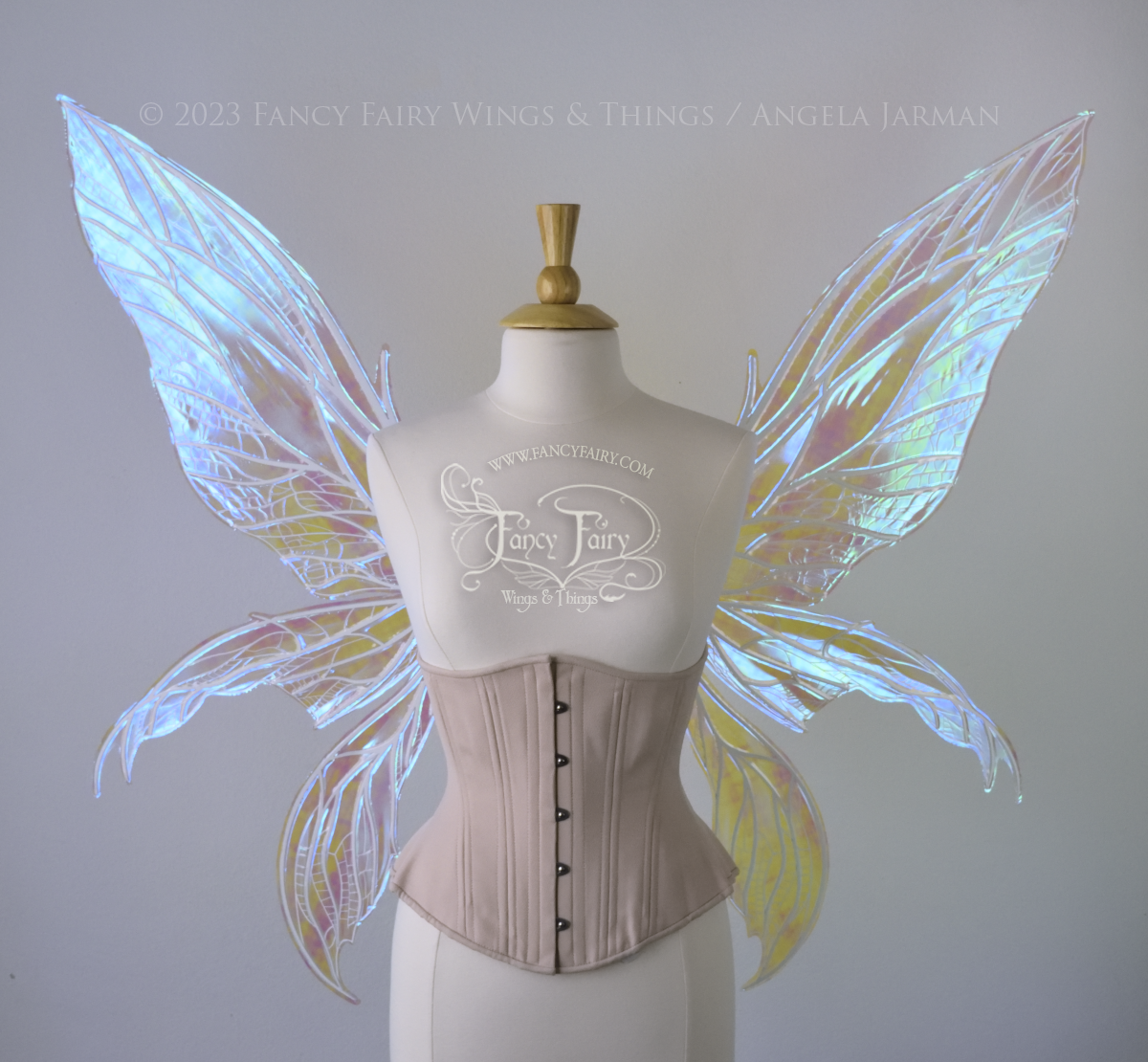 Front view of an ivory dress form wearing an underbust corset and large blue/teal/violet iridescent fairy wings. Upper panels are elongated with pointed tips, 2 lower panels curve downward, detailed white veins 