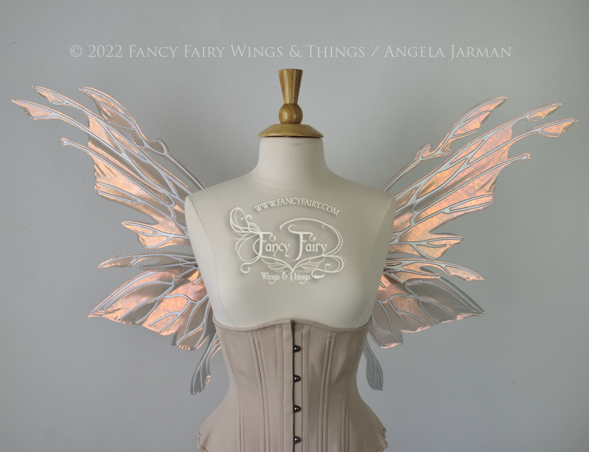 Front view of an ivory dress form wearing an alabaster underbust corset & large rose gold iridescent fairy wings with elongated upper panels with petal like appendages at the tips & antennae, the veins are white