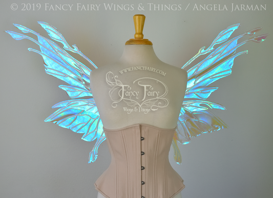 Front view of an ivory dress form wearing an alabaster underbust corset & clear opal blue iridescent fairy wings with elongated upper panels with petal like appendages at the tips & antennae, the veins are white