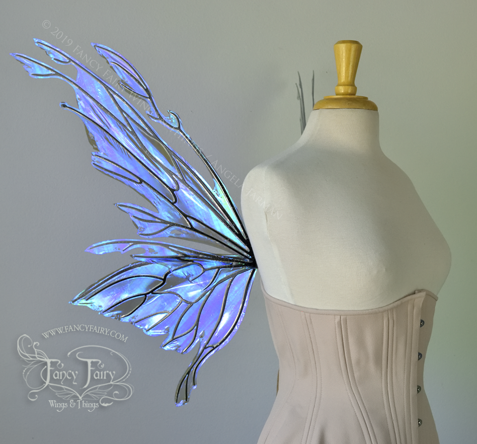 Left side view of an ivory dress form wearing an alabaster underbust corset & purple / blue iridescent fairy wings with elongated upper panels with petal like appendages at the tips & antennae, the veins are black