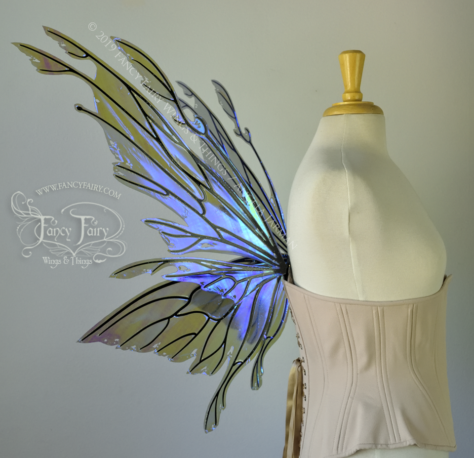 Left side view of an ivory dress form wearing an alabaster underbust corset & purple / blue iridescent fairy wings with elongated upper panels with petal like appendages at the tips & antennae, the veins are black