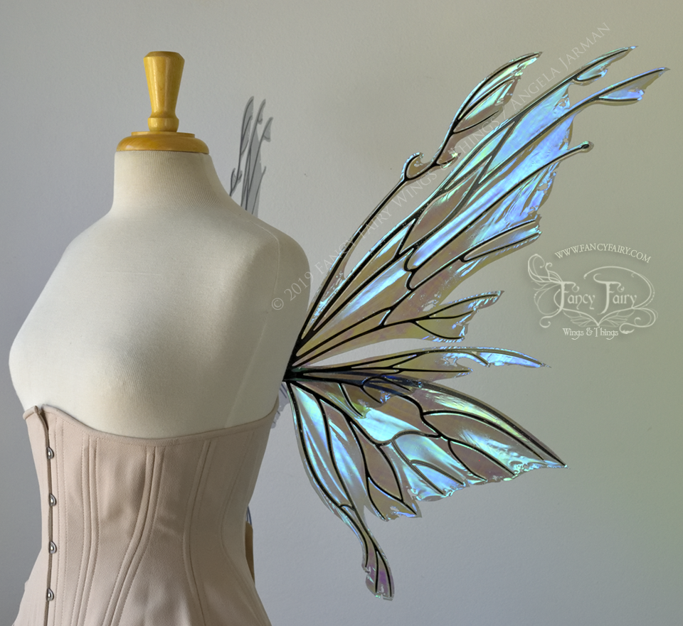 Right side view of an ivory dress form wearing an alabaster underbust corset & purple / blue iridescent fairy wings with elongated upper panels with petal like appendages at the tips & antennae, the veins are black