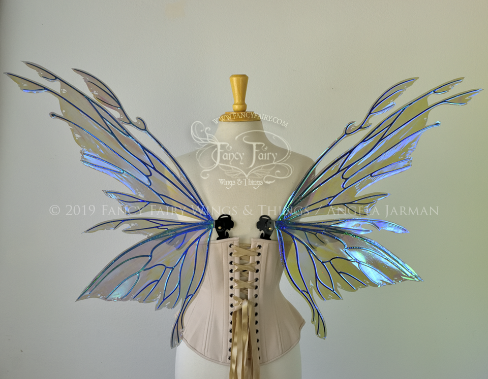 Back view of an ivory dress form wearing an alabaster underbust corset & purple / blue iridescent fairy wings with elongated upper panels with petal like appendages at the tips & antennae, the veins are black