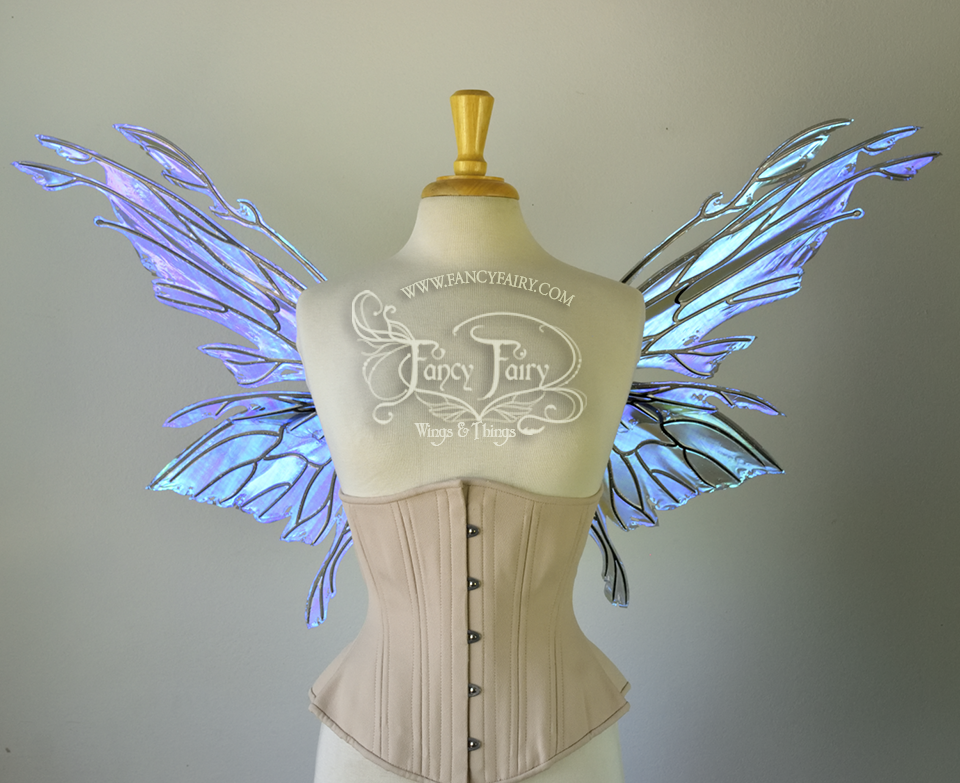 Front view of an ivory dress form wearing an alabaster underbust corset & purple / blue iridescent fairy wings with elongated upper panels with petal like appendages at the tips & antennae, the veins are black