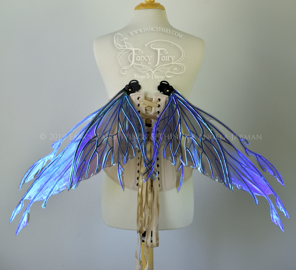 Back view of an ivory dress form wearing an alabaster underbust corset & purple / blue iridescent fairy wings with elongated upper panels with petal like appendages at the tips & antennae, the veins are black. Wings are in resting position