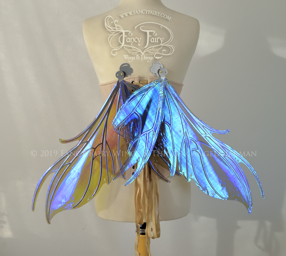 Back view of a dress form wearing an underbust corset & purple / blue iridescent fairy wings with a spikey shape, with silver veins, in resting position