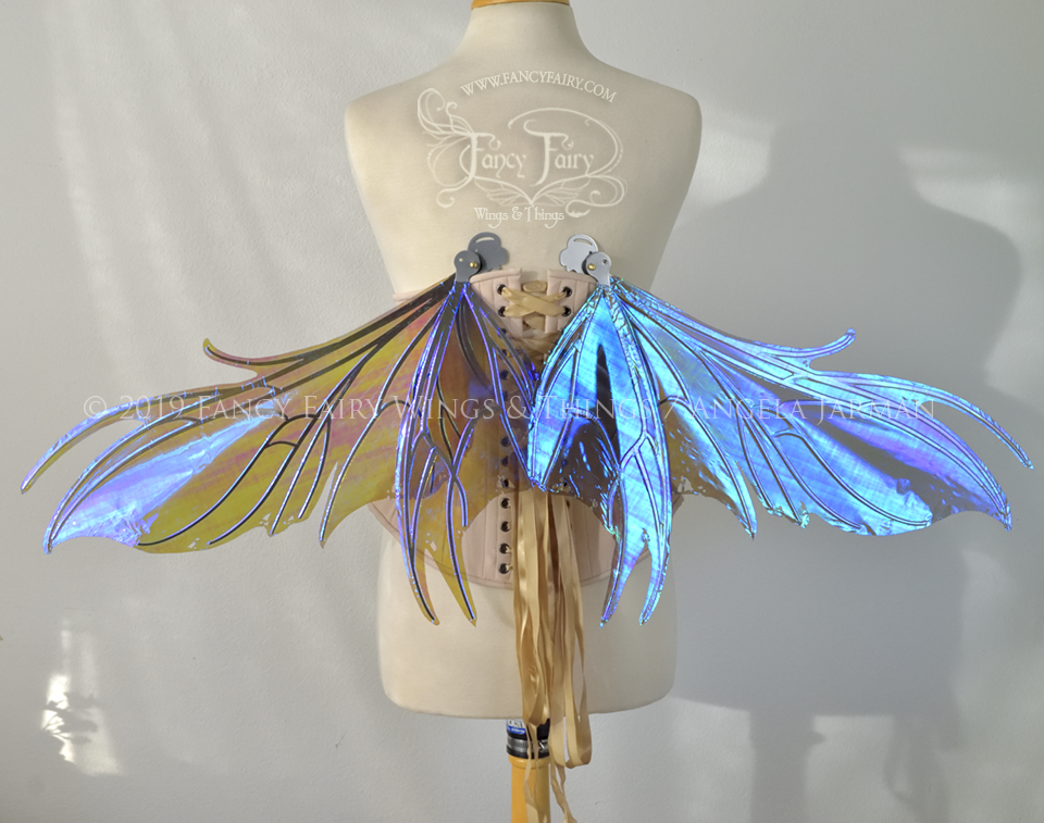 Back view of iridescent blue / purple fairy wings in partial resting position, with spikey silver veins, worn by a dress form