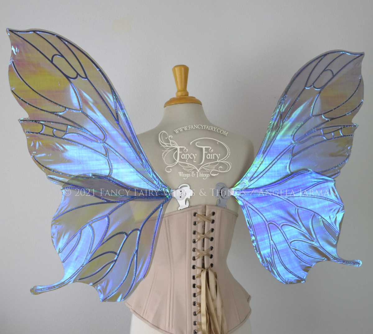 Back view of an ivory dress form wearing an alabaster underbust corset & large purple / blue iridescent fairy wings with a sort of butterfly shape. The veins are silver