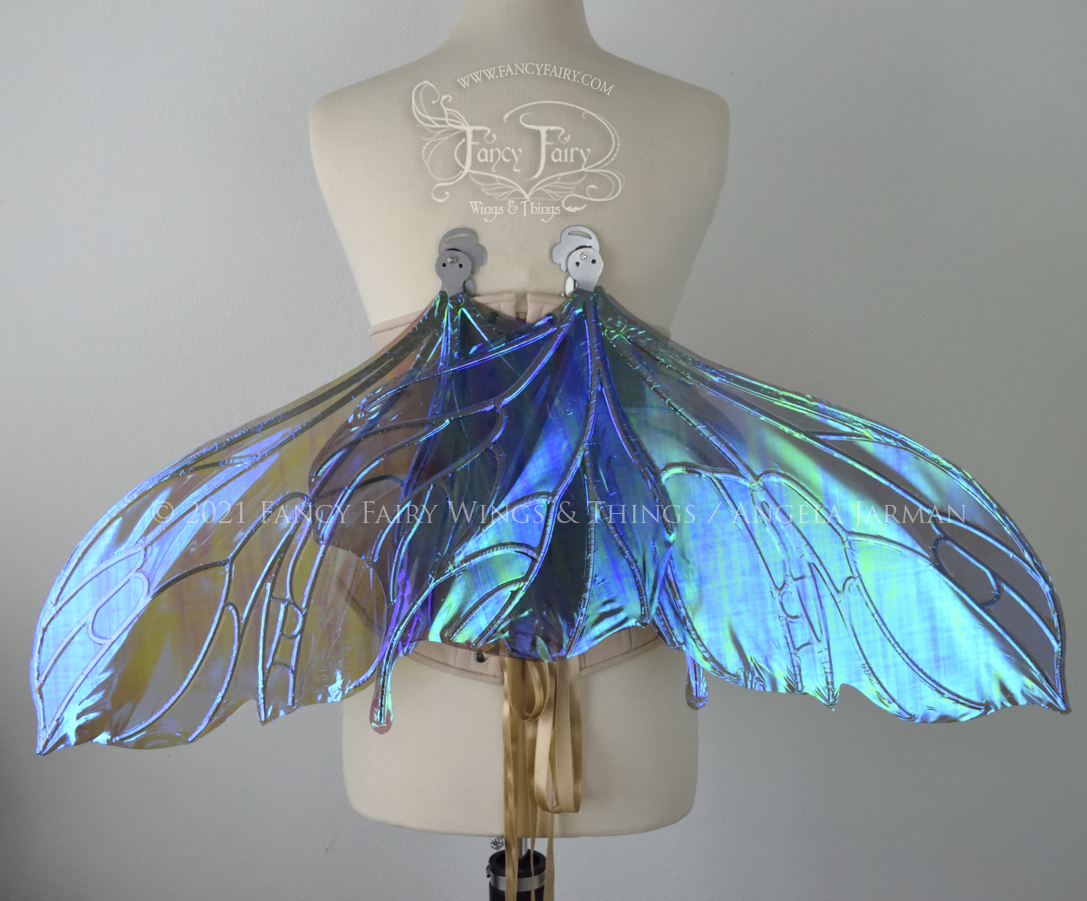 Back view of an ivory dress form wearing an alabaster underbust corset & large purple / blue iridescent fairy wings with a sort of butterfly shape. The veins are silver, wings are lowered in resting position