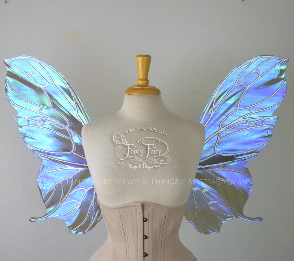 Front view of an ivory dress form wearing an alabaster underbust corset & large purple / blue iridescent fairy wings with a sort of butterfly shape. The veins are silver