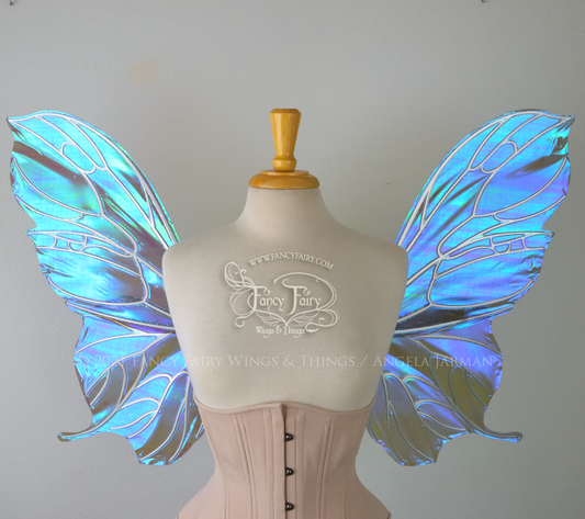 Front view of an ivory dress form wearing an alabaster underbust corset & large purple / blue iridescent fairy wings with a sort of butterfly shape. The veins are silver