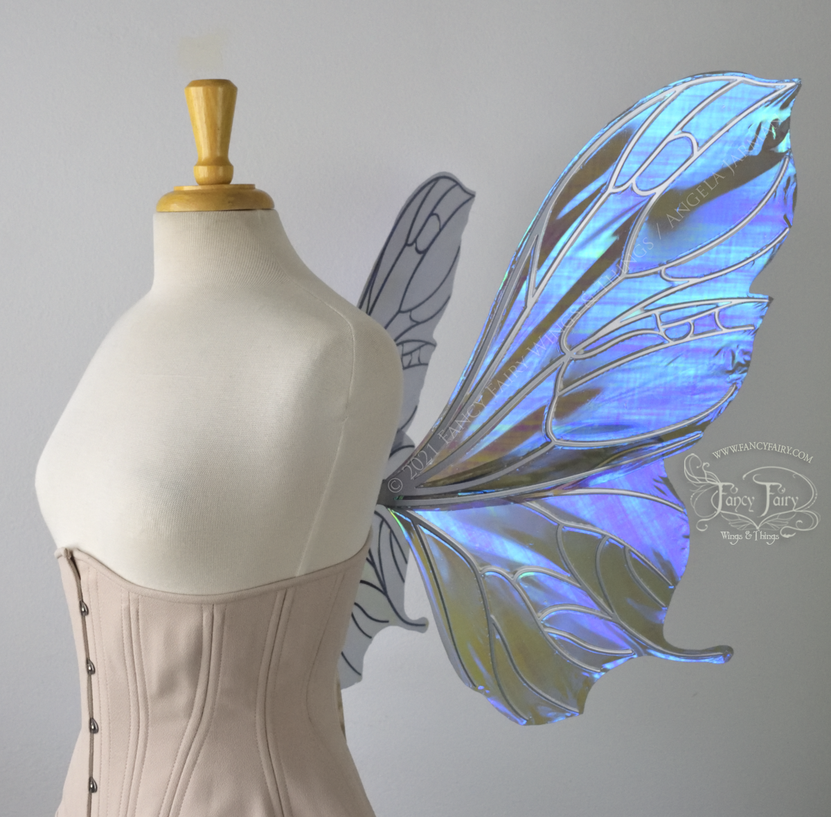 Right side view of an ivory dress form wearing an alabaster underbust corset & large purple / blue iridescent fairy wings with a sort of butterfly shape. The veins are silver