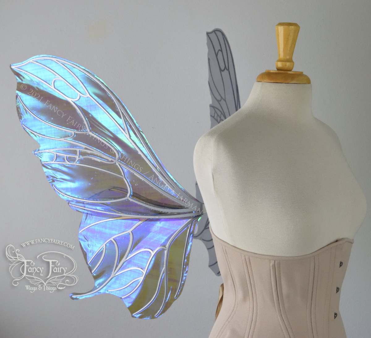 Left side view of an ivory dress form wearing an alabaster underbust corset & large purple / blue iridescent fairy wings with a sort of butterfly shape. The veins are silver