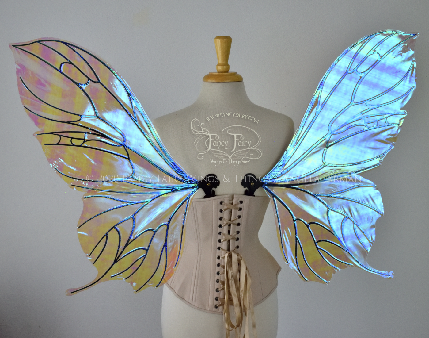 Back view of an ivory dress form wearing an alabaster underbust corset & large blue opal iridescent fairy wings with a sort of butterfly shape. The veins are black