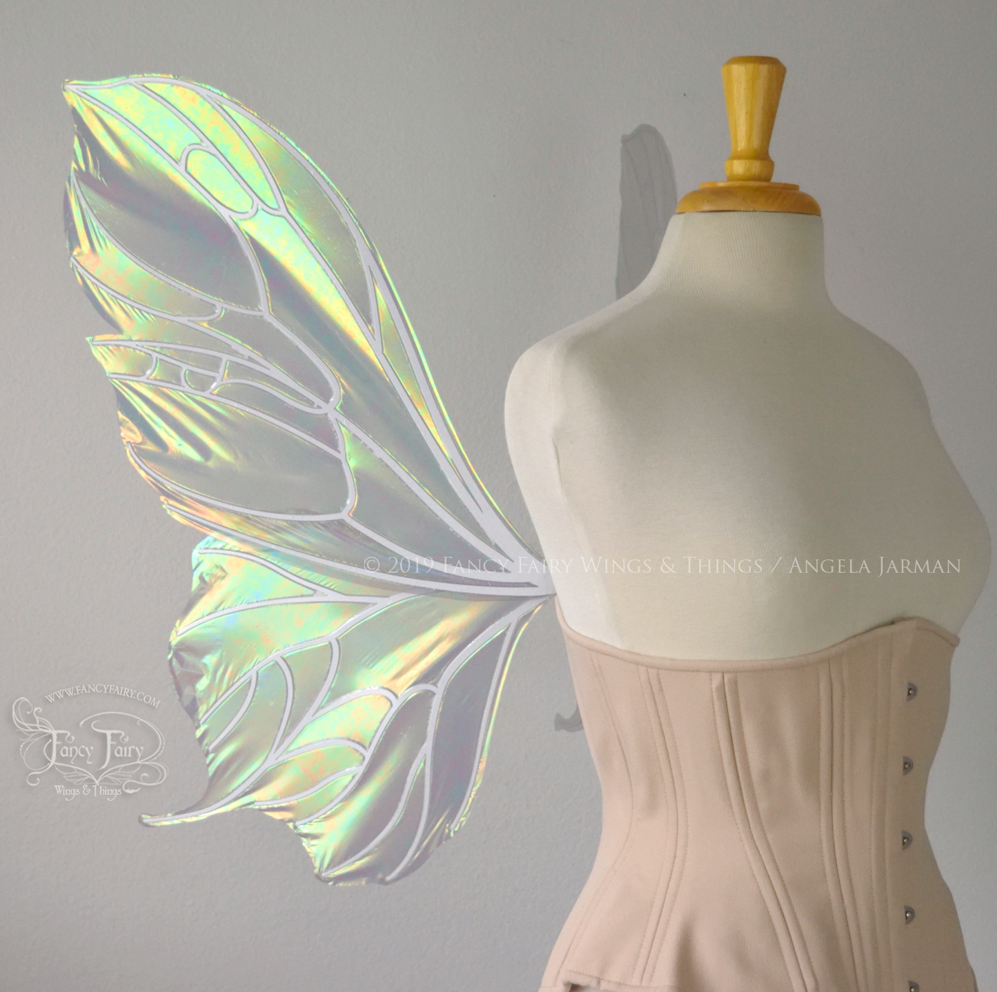 Left side view of an ivory dress form wearing an alabaster underbust corset & large iridescent fairy wings with a sort of butterfly shape. The veins are white