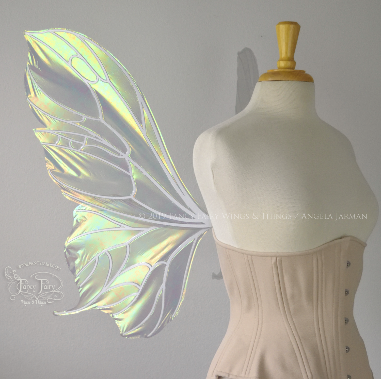 Left side view of an ivory dress form wearing an alabaster underbust corset & large iridescent fairy wings with a sort of butterfly shape. The veins are white